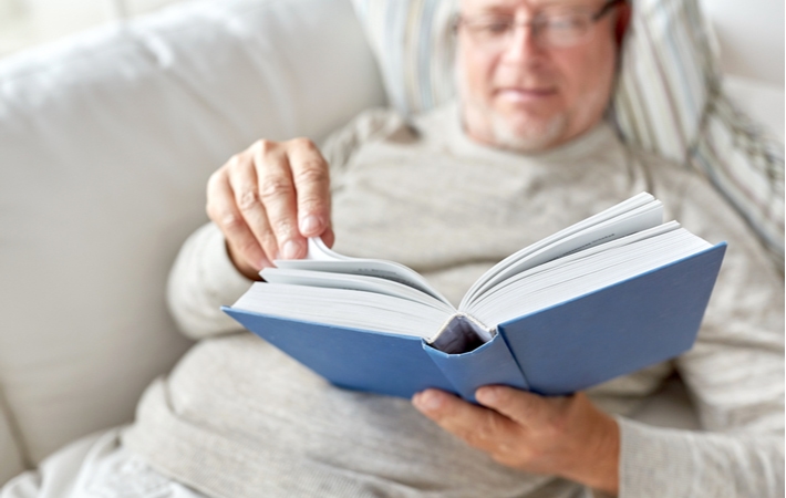 A close up of a book that a senior man is reading, turning to the next page while he lays down