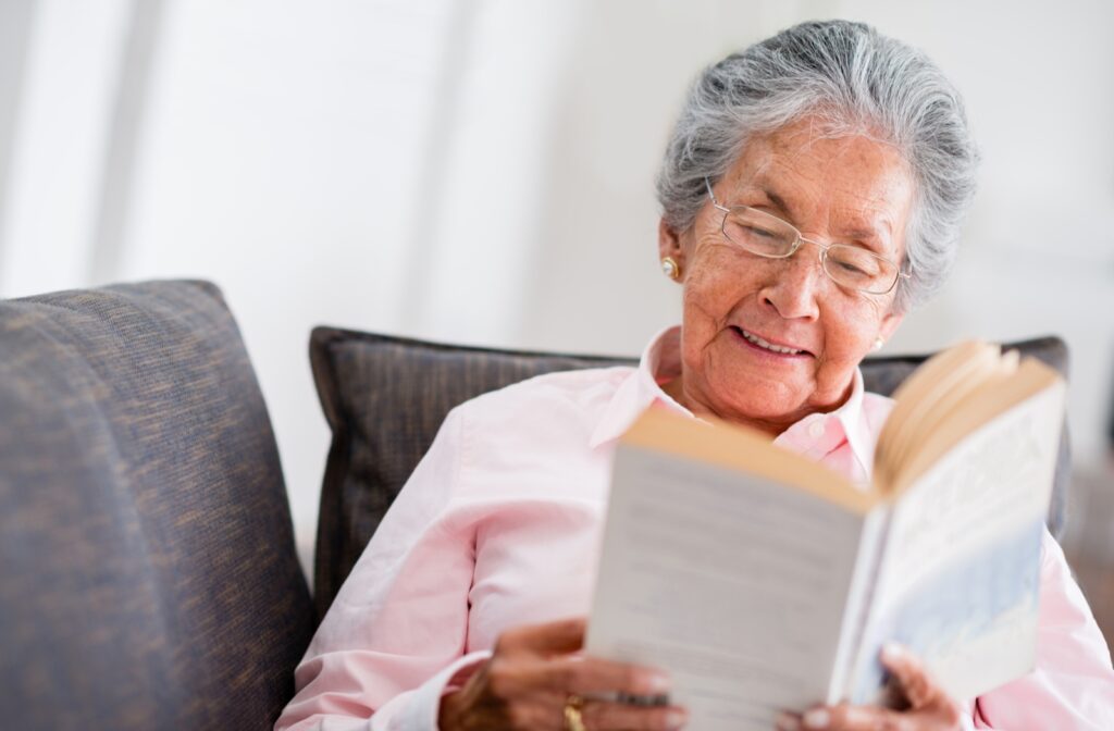 A senior woman sitting on a sofa smiling while she reads a book