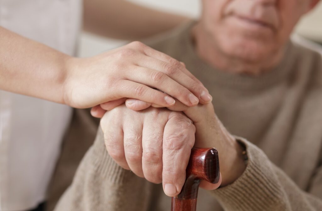 A caregiver resting her hand on top of a senior man's hands who is holding a cane