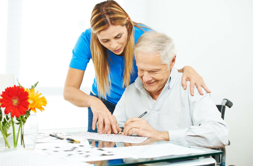 A senior man in does a crossword with a memory support caregiver