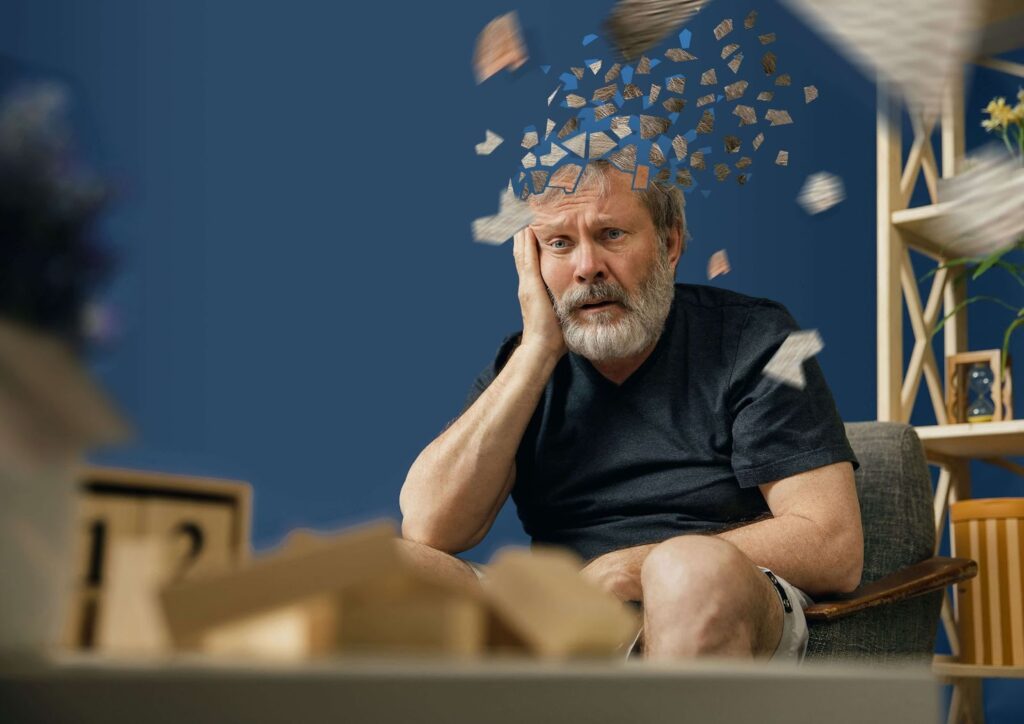 An elderly man is sitting on a chair and is feeling frustrated in remembering something. Head getting scattered and fading away, an illustration of declining memory.