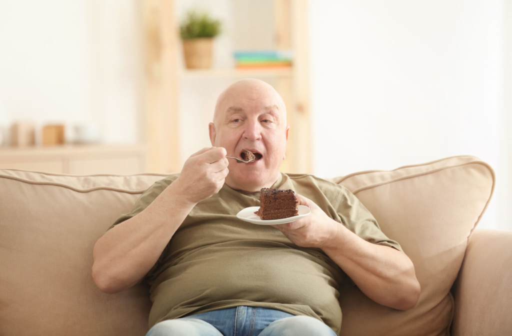 An older man sitting on a couch eating a piece of chocolate cake.